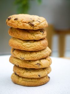 A stack of homemade chocolate chip cookies on a white plate, ready to be served.